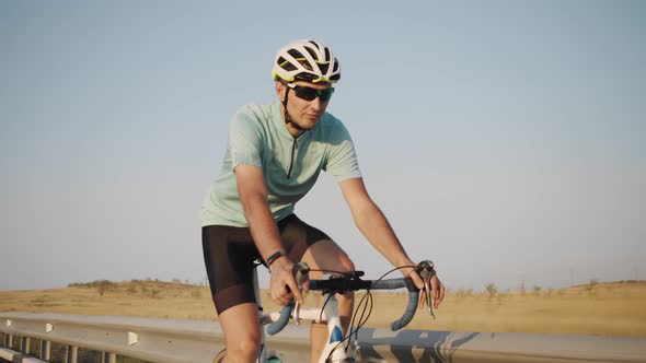 Male Cyclist in Helmet and Sunglasses Rides Bicycle Along Highway Closeup alt