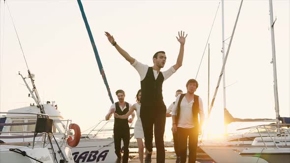 A Group of Young Street Artists Running Along the Path Along the Pier They Laugh alt