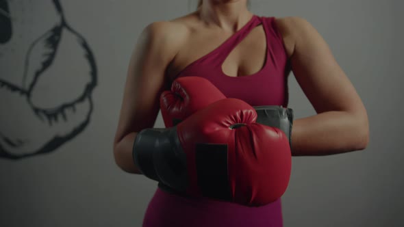 A sporty woman puts boxing gloves on her hands before training in the gym alt