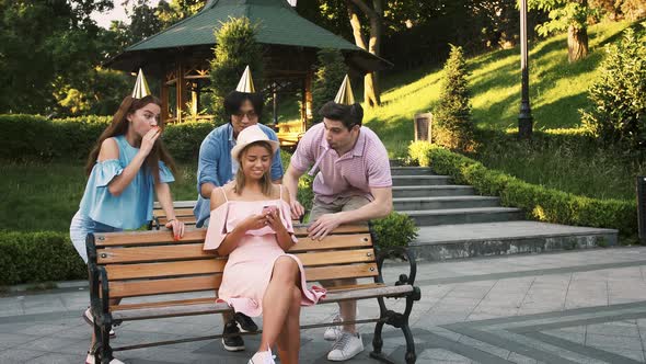 Young Birthday Woman Using Smartphone Sitting on Bench in Park alt