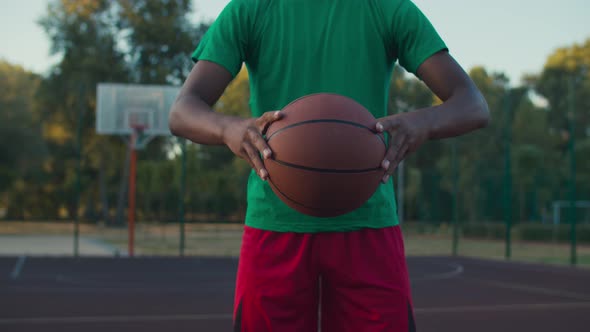Basketball Player Holding Ball Outdoors at Sunrise alt