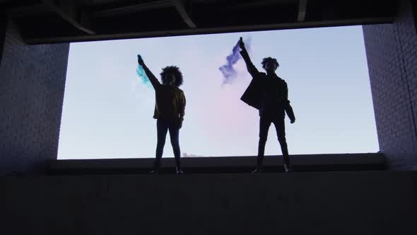 Mixed race man and woman holding blue and purple flares standing in an empty building alt
