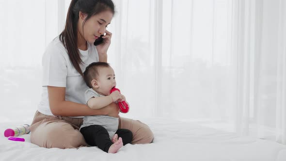 Happy Asian mom and baby newborn sitting and using a smartphone