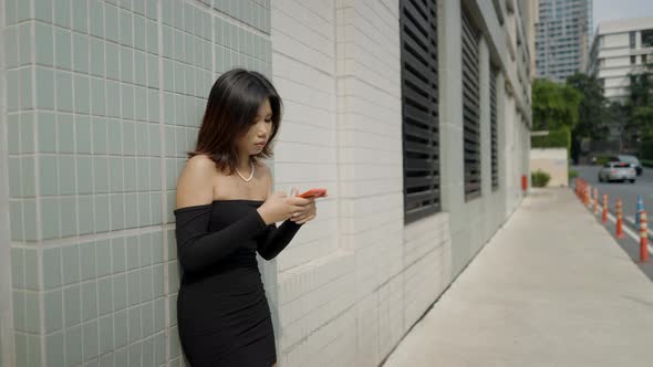 Beautiful Young Asian Woman in a Black Sexy Dress Texting on a Red Phone in a Empty Street of alt