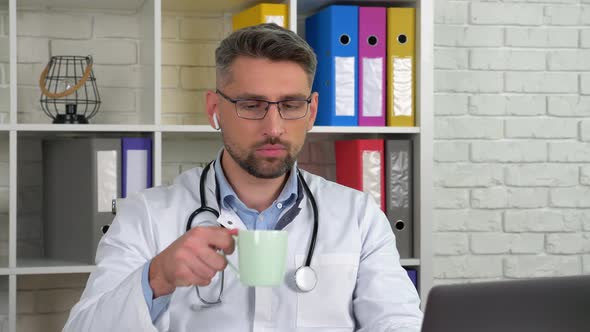 Doctor listens patient online video call laptop webcam, drinking coffee tea alt