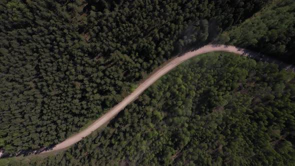 Aerial footage of a red car speeding trough dusty forest road