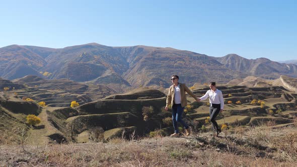 Young Couple Holding Hands is Walking on the Background of Mountain Terraces on a Sunny Day alt
