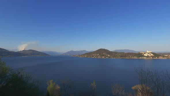 Panoramic view over Maggiore lake and smoke from mountain due to burning fire close to Nebbiuno in P alt