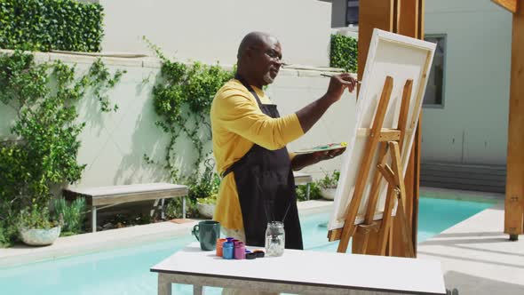 African american senior man standing on a terrace and painting alt