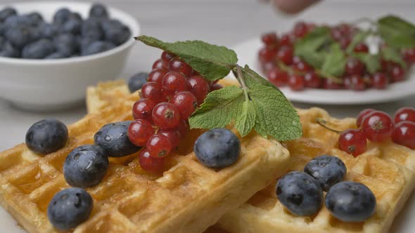 The chef puts a mint leaf on a plate of maple syrup-poured waffles garnished with berries alt