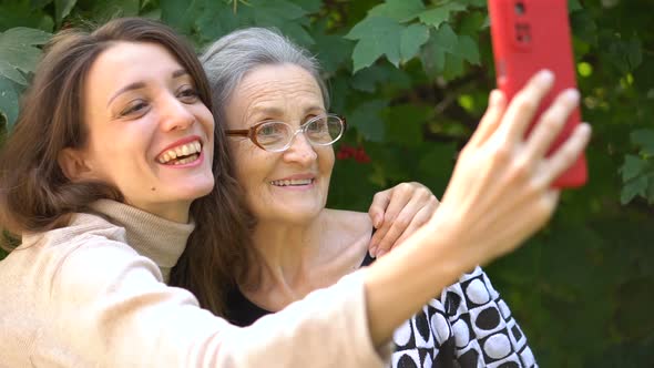 Adult Daughter and Senior Mum are Taking Selfportrait Picture Selfie on Red Smartphone Together alt