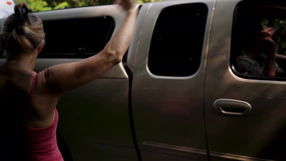 Mature woman throwing kisses and waving to an elderly couple in a pickup truck pulling an RV. alt