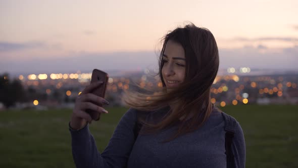 Woman Using Smartphone in Park with City Lights in Background