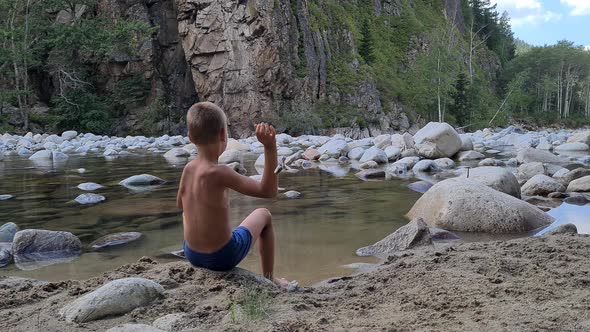 a boy plays on the riverbank, throws stones into the water