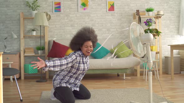 African Woman with an Afro Hairstyle in Front of the Fan Is Saved From Heat alt
