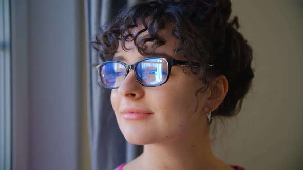 Video portrait of pretty brunette female in nerd glasses looking in window at home in 4k video alt