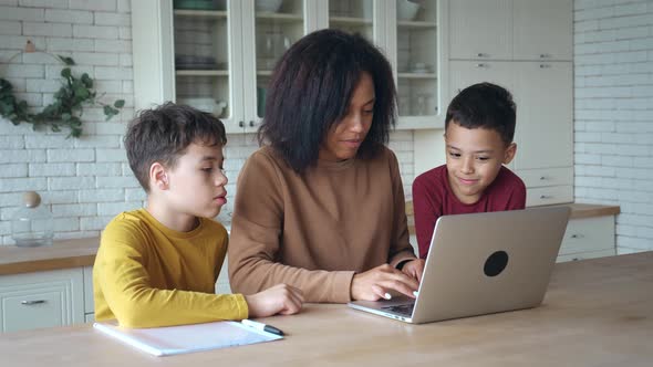 Smiling African American Mother and Kids Sons Having Fun with Computer Sitting at the Kitchen Table alt
