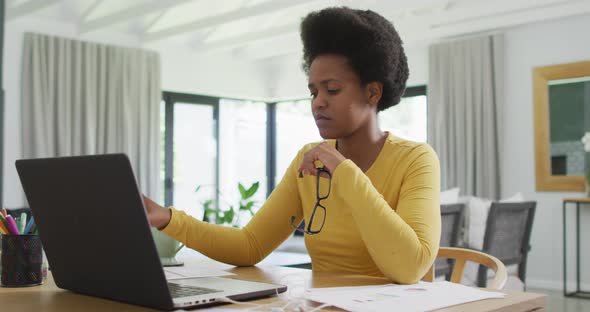 Tired african american woman sitting at table using laptop alt