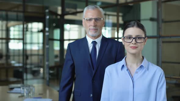 Young Woman and Mature Man Folding Arms Looking Camera alt