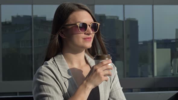 Smiling Young Woman in Sunglasses Drinks Coffee From a Disposable Cup
