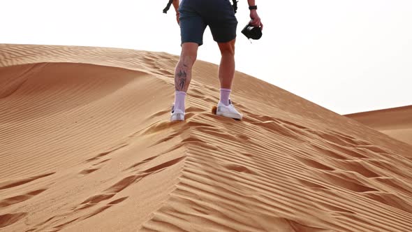 Man With Backpack Hiking Up Sand Dune In Desert alt