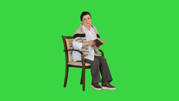 Happy Senior Woman Reading a Book Aloud on Camera on a Green Screen Chroma Key alt
