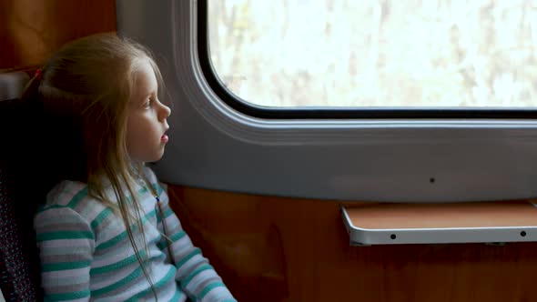Happy Little Child Girl Looks Out Window of Train in Carriage
