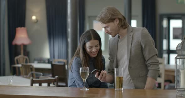 Man holding mobile phone and talking with woman in pub