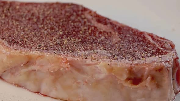 Close Slow Motion Slider Shot of Seasoning a Raw New York Strip Steak With Cracked Black Pepper alt