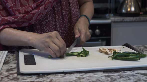 Hands Of Ethnic Minority Female Chopping Fresh Green Chillies On A Board. Locked Off alt