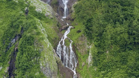The Flow of Water Falls From a Cliff Overgrown with Trees alt