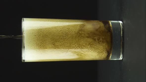 Vertical Video Cola is Poured Into Glass Full of Bubbles and Foam Isolated on Black Background