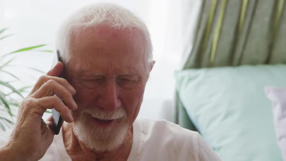 Senior man in social distancing talking by phone in his room alt
