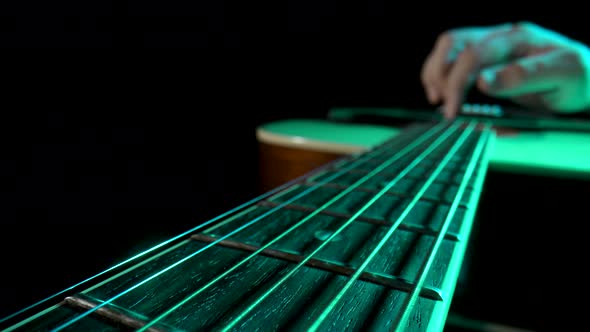 Man Musician Plays a Wooden Acoustic Guitar on a Black Background with Green Light alt