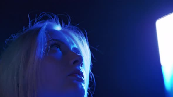 The Face of a Young Adorable Woman is Directed Upward Towards a Brightly Glowing Advertising Screen alt
