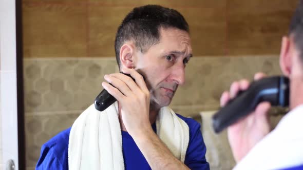 Mature adult man is shaving face with electric razor alt