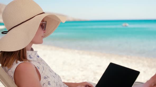 Rich Woman Talks Online Via Internet Video Call Using Laptop on Sea Beach Sunbed