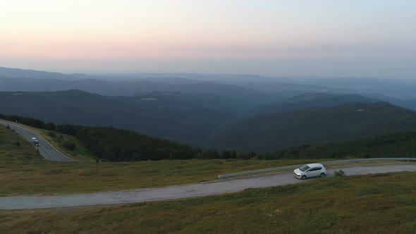 Aerial View of Cars Driving on Mountain Highway Pass with Deep Valley Bellow at Sunset alt