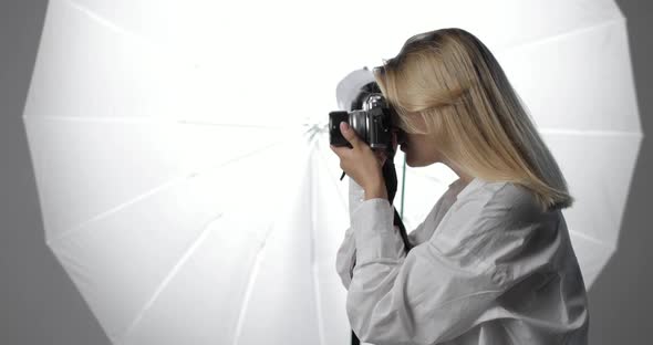 Beautiful Young Woman Photographer in a White Shirt with Long Blond Hair is Working Making Shots
