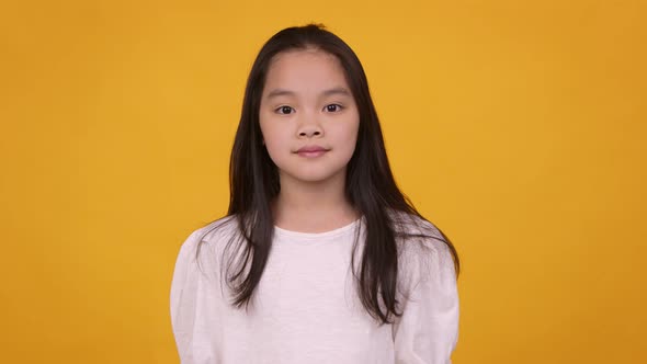 Studio Portrait of Cute Asian Girl Looking at Camera Orange Background alt