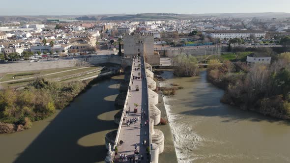 Aerial forward view of Cordoba old roman bridge over river Guadalquivir with people. Andalucia, Spai
