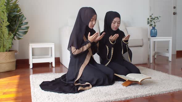 Young Muslim woman and female friend reading Quran and praying