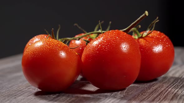Appetizing Red Juicy Tomatoes on a Branch with Water Drops Lie on a Wooden Surface and Spin alt