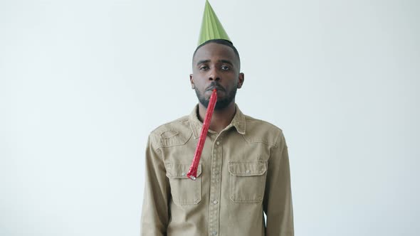Slow Motion Portrait of African American Man Wearing Bright Hat Blowing Party Horn with Miserable alt