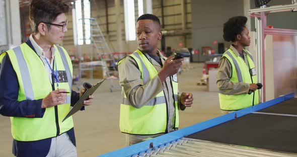 Diverse male and female workers talking next to conveyor belt in warehouse alt