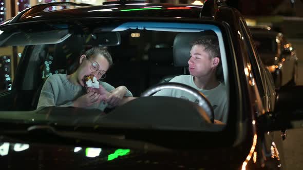 Two young people - a guy and a young woman have fun and eat a burger in the car alt
