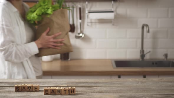 Save The Earth Lined With Cubes On Kitchen Table. Woman Carries Paper Bag, Places It Near alt