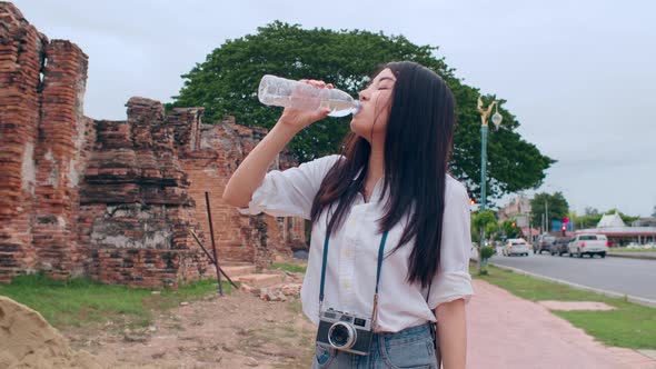 woman blogger tourist with camera feel tired stand in front of pagoda take a rest and drink water.