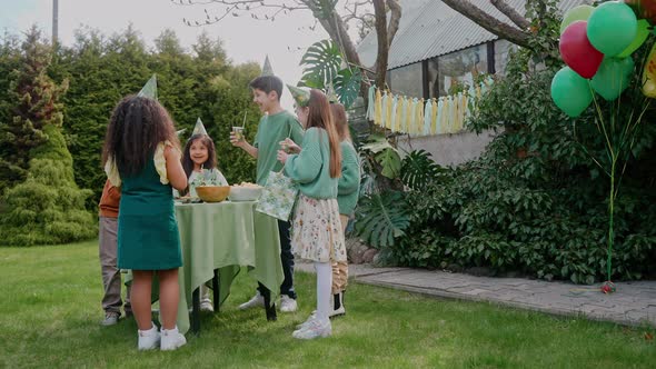 Kids Having a Greenthemed Birthday Party at the Backyard Eating at the Table