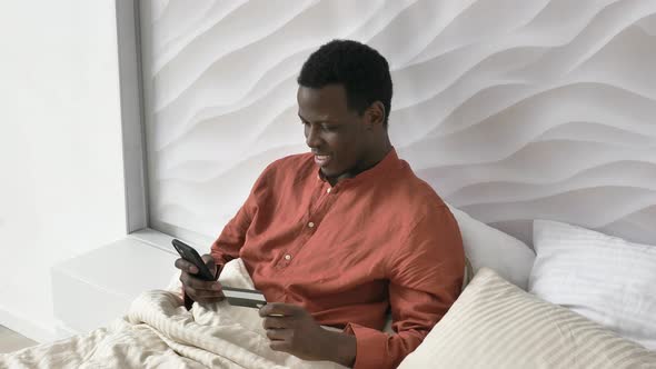 AfricanAmerican Man Pays Online with Phone and Credit Card alt
